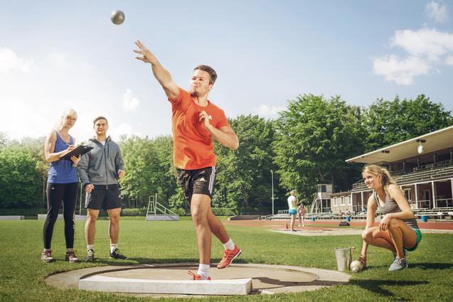 Ein Mann stößt eine Kugel im Stadion, drei Personen beobachten und messen daneben