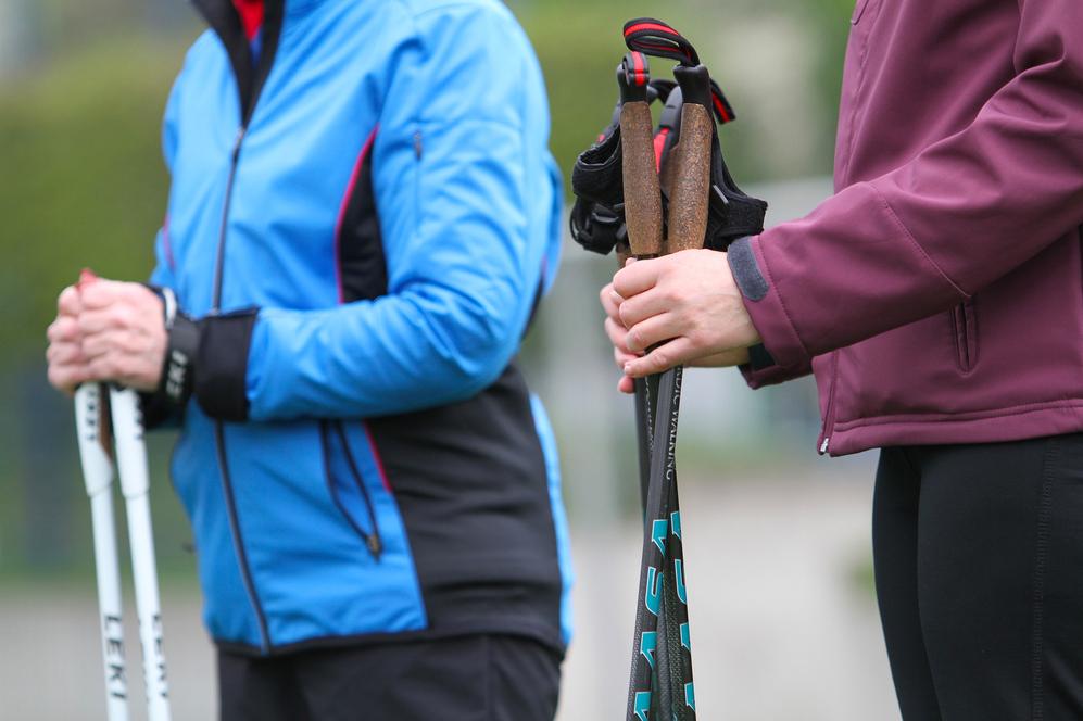 Nahaufnahme von zwei Personen, die Wanderstöcke halten, eine in einer blauen, die andere in einer burgunderfarbenen Jacke.