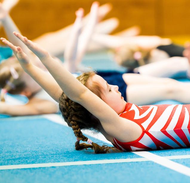 Mädchen mit Zöpfen liegt auf einer blauen Gymnastikmatte und hebt die Arme während eines Trainings.